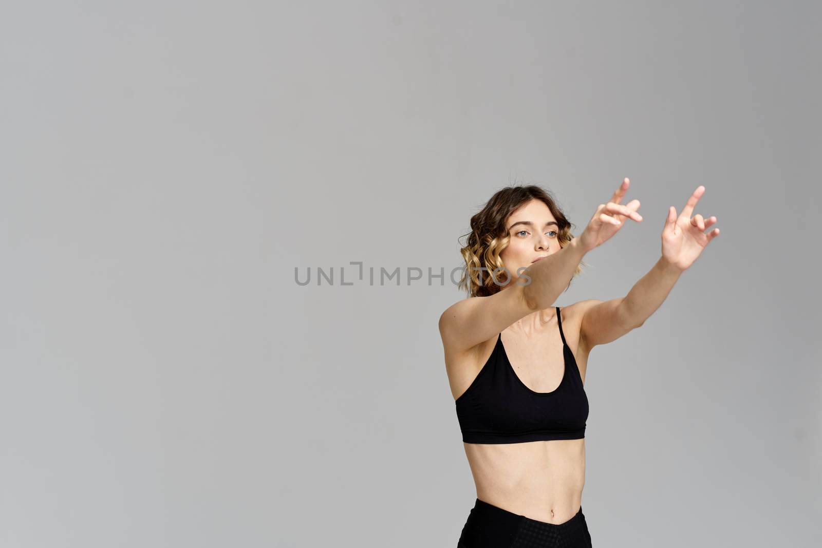 A slender woman in black leggings on a gray background gestures with her hands gymnastics sports. High quality photo