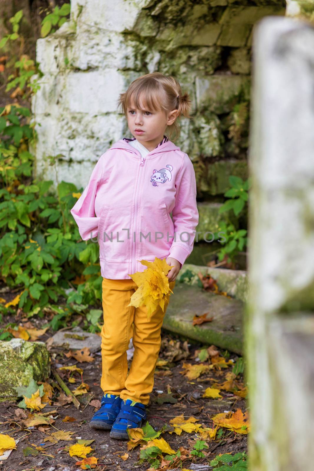 A girl with a broken arm stands near a brick wall in an old park on an autumn walk