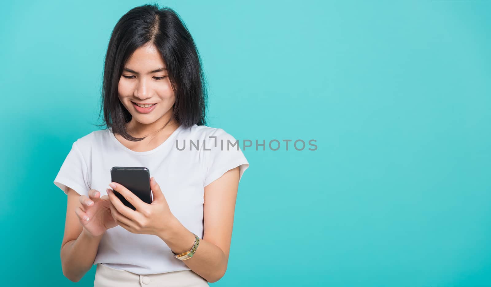 Portrait Asian beautiful happy young woman standing smile holding using mobile smart phone looking to smartphone, shoot the photo in a studio on a blue background, There was copy space