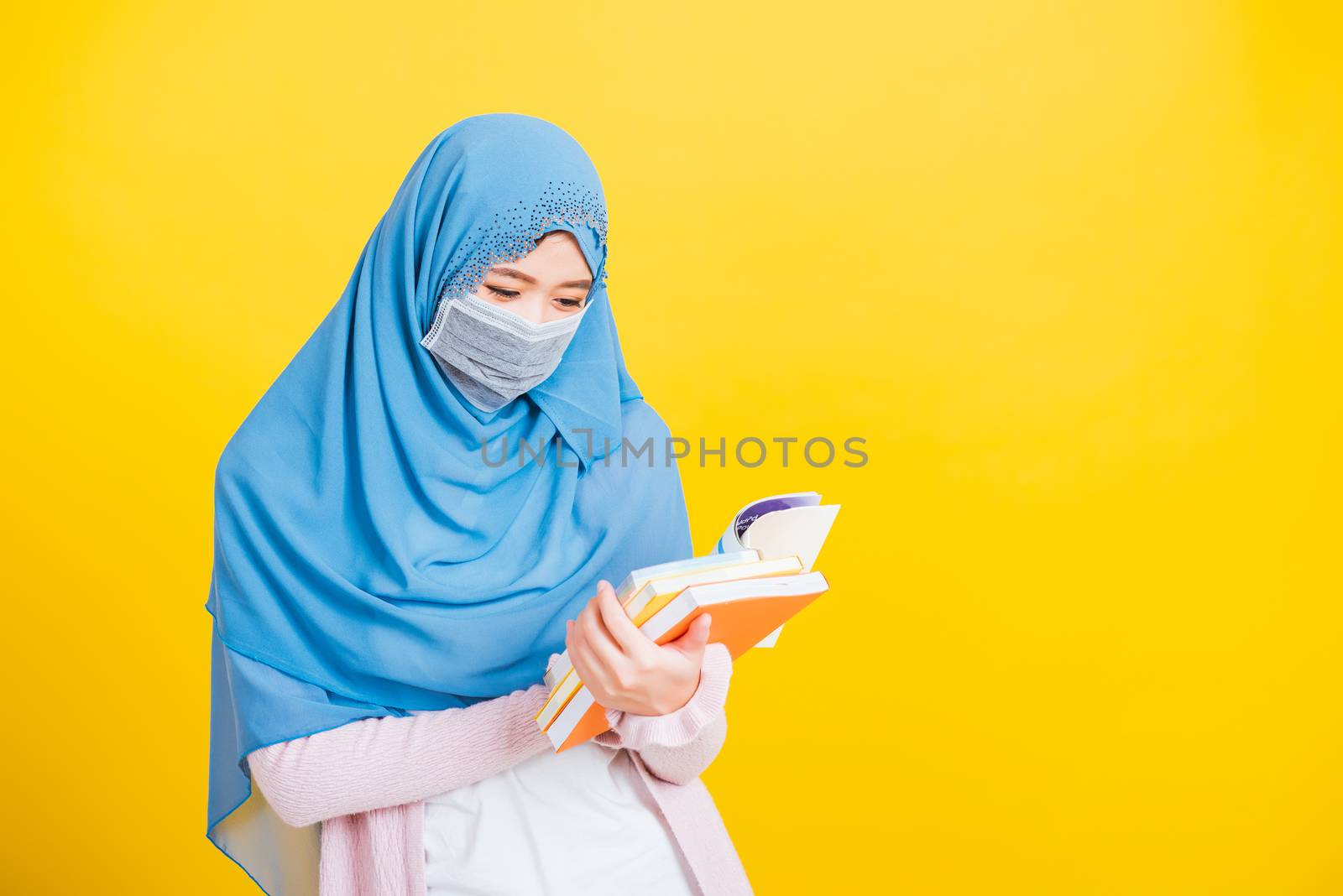 Asian Muslim Arab, Portrait of happy beautiful young woman religious wear veil hijab and face mask protective to prevent coronavirus she hold book on hand and open reding it on yellow, Back to college