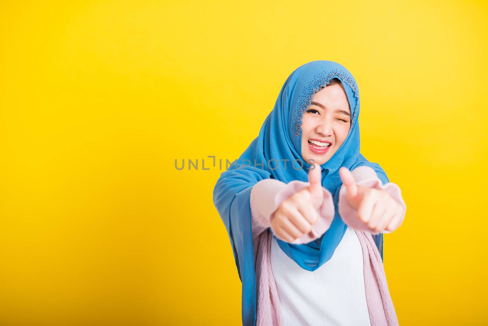 Asian Muslim Arab, Portrait of happy beautiful young woman Islam religious wear veil hijab funny smile she made finger thumbs up, Ok sign to agree, studio shot isolated on yellow background