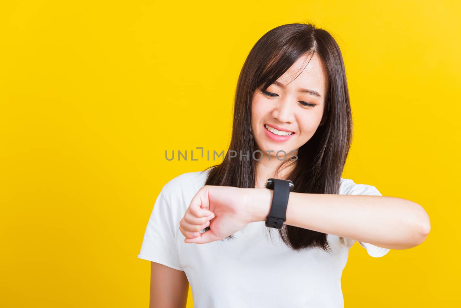 Portrait Asian of a happy beautiful young woman smiling looking and pointing finger her smart wristwatch studio shot isolated on yellow background