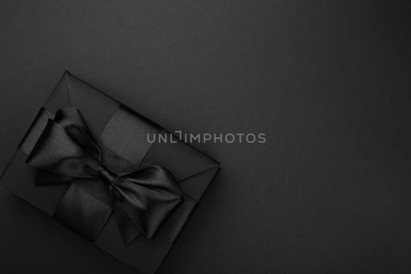 Black friday gift, paper box with silk ribbon bow on black paper background with copy space for text, flat lay top view template