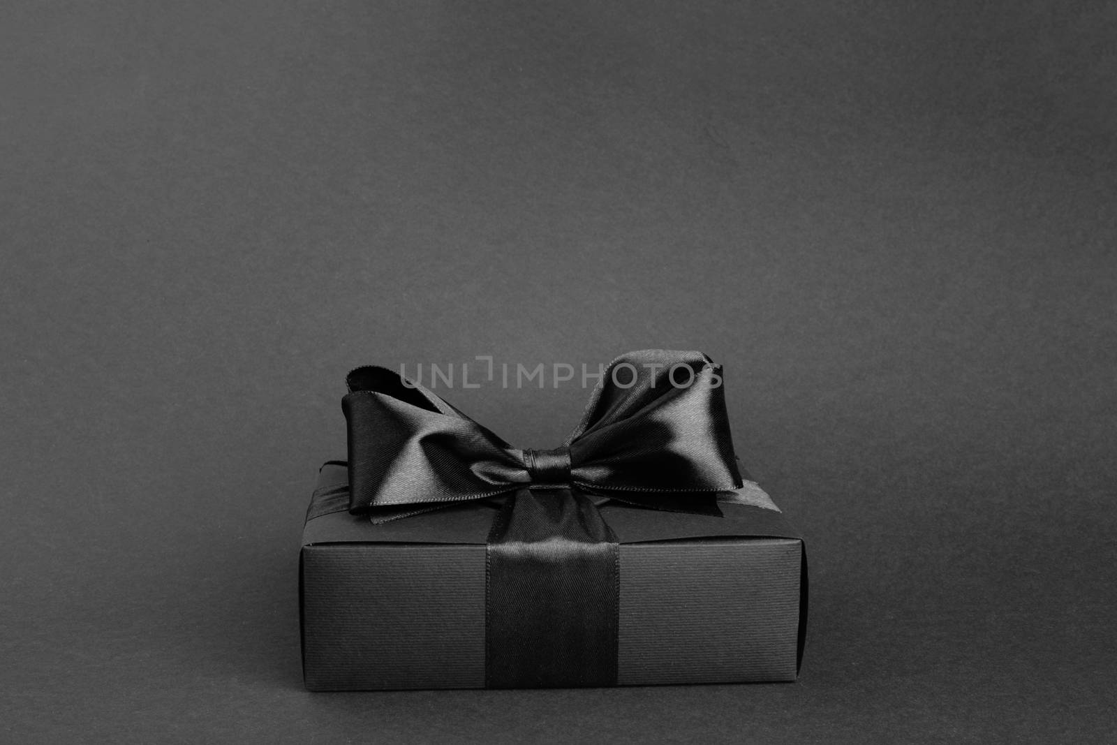 Black friday gift, paper box with silk ribbon bow on black background