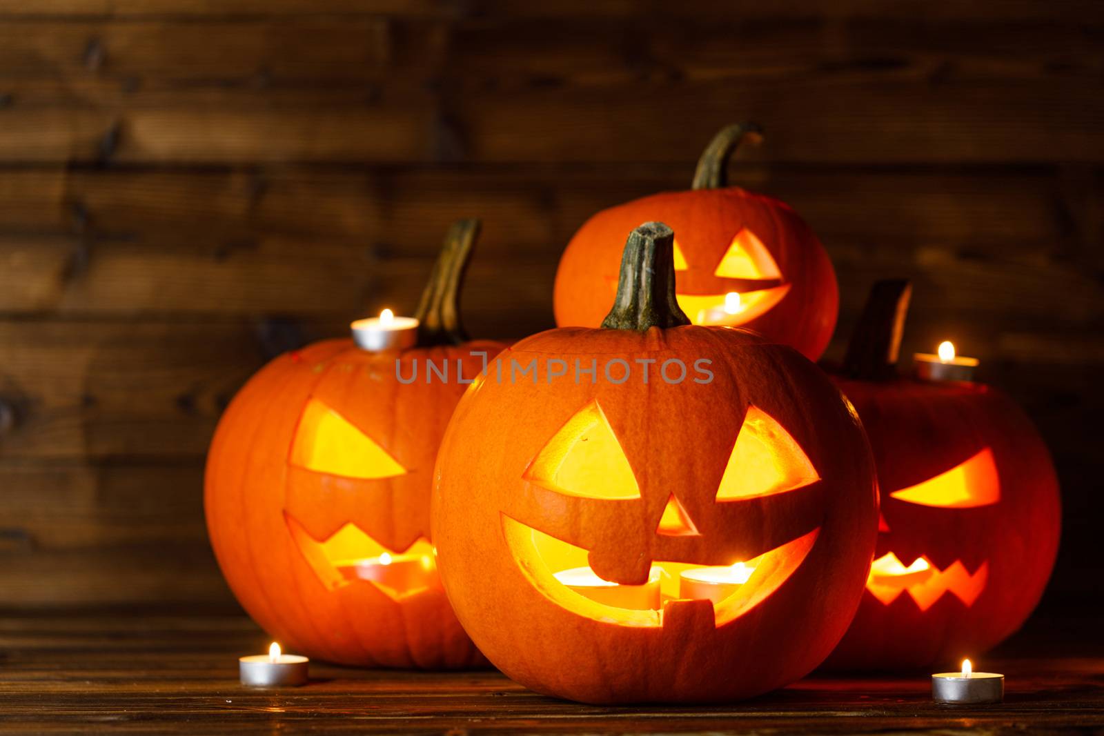 Halloween pumpkin head lanterns and burning candles on wooden background