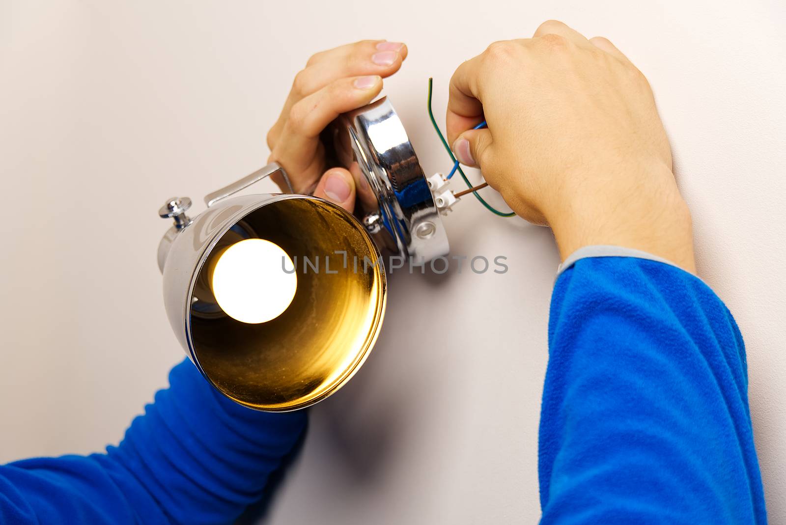 Male electrician connects the lamp on the wall. by PhotoTime