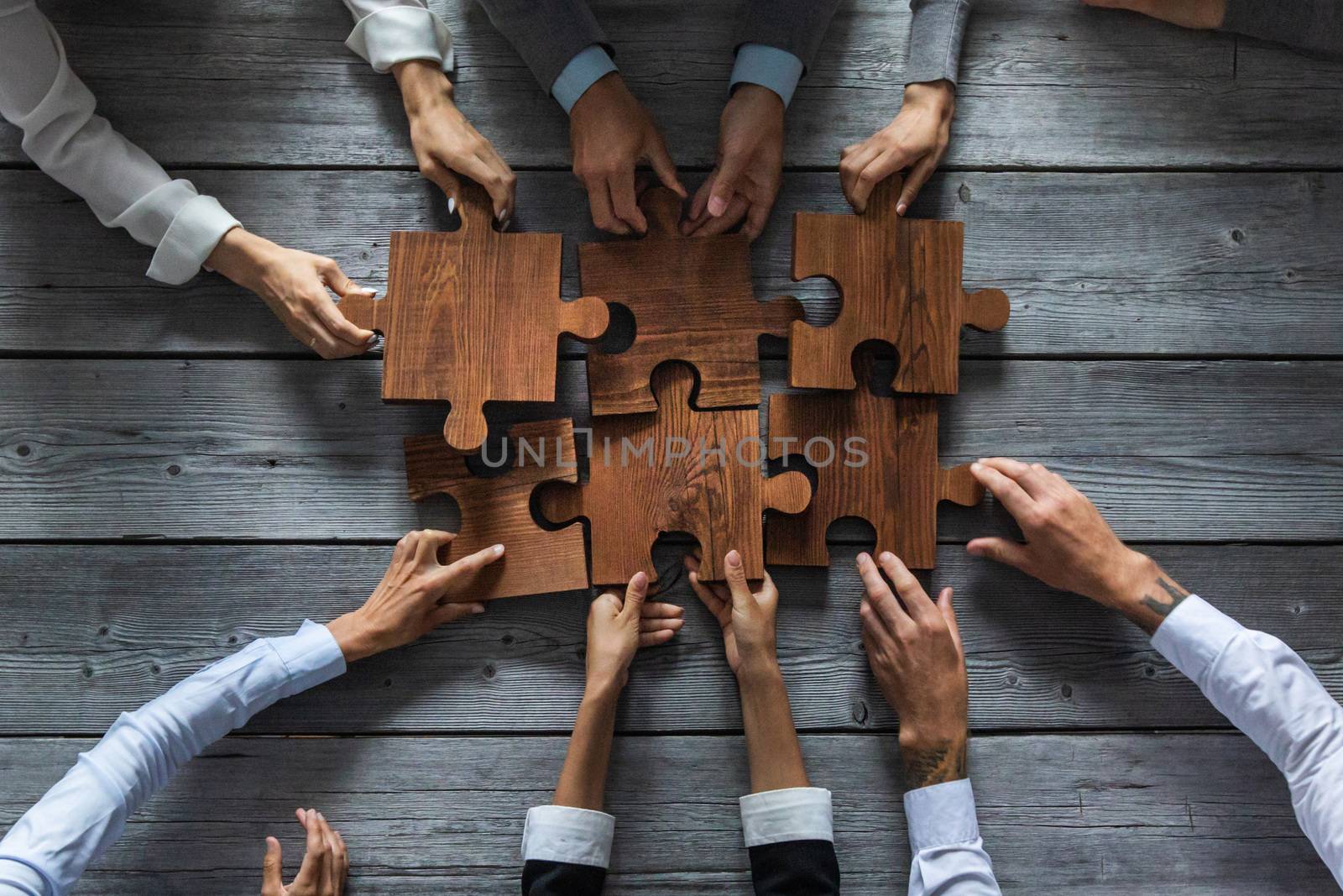 Business people team sitting around meeting table and assembling wooden jigsaw puzzle pieces unity cooperation ideas concept