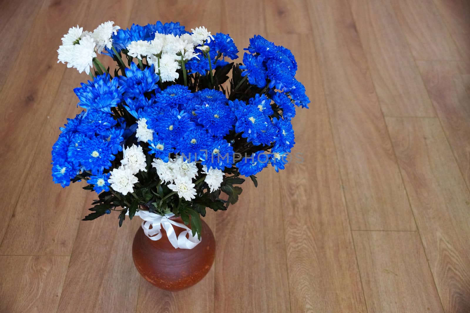 a bouquet of blue and white chrysanthemums in a clay vase on the wooden floor