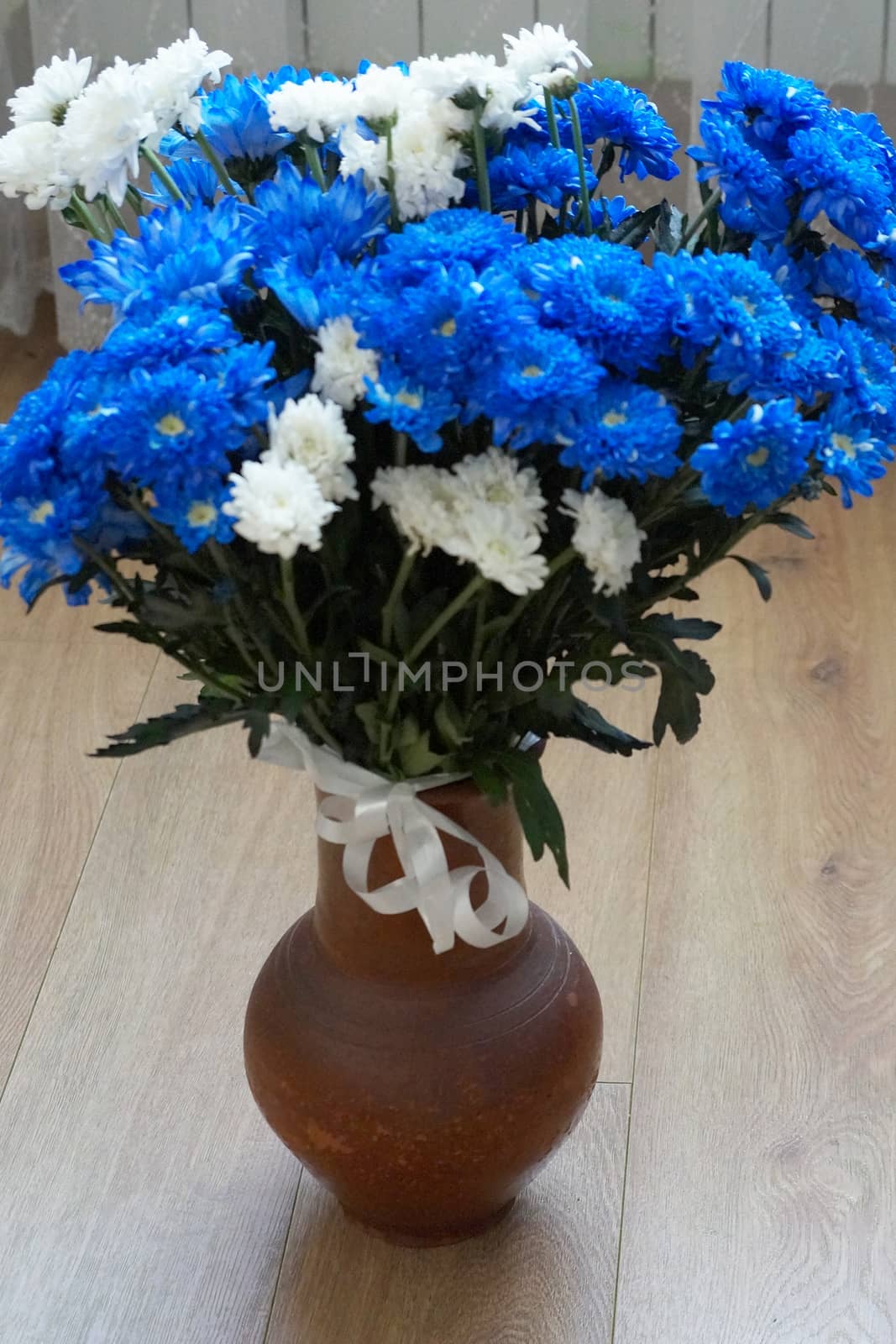 a bouquet of blue and white chrysanthemums in a clay vase on the wooden floor
