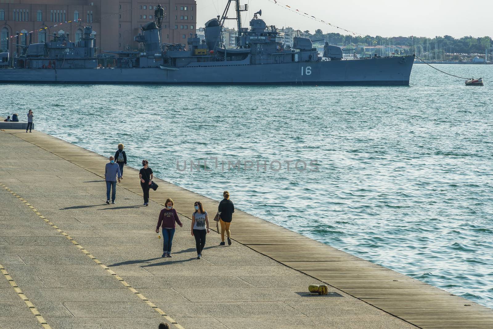 Unidentified persons with face protection walk on the pedestrian area of the city waterfront.