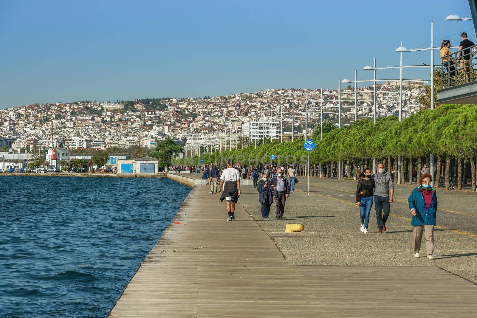 Unidentified persons with face protection walk on the pedestrian area of the city waterfront.