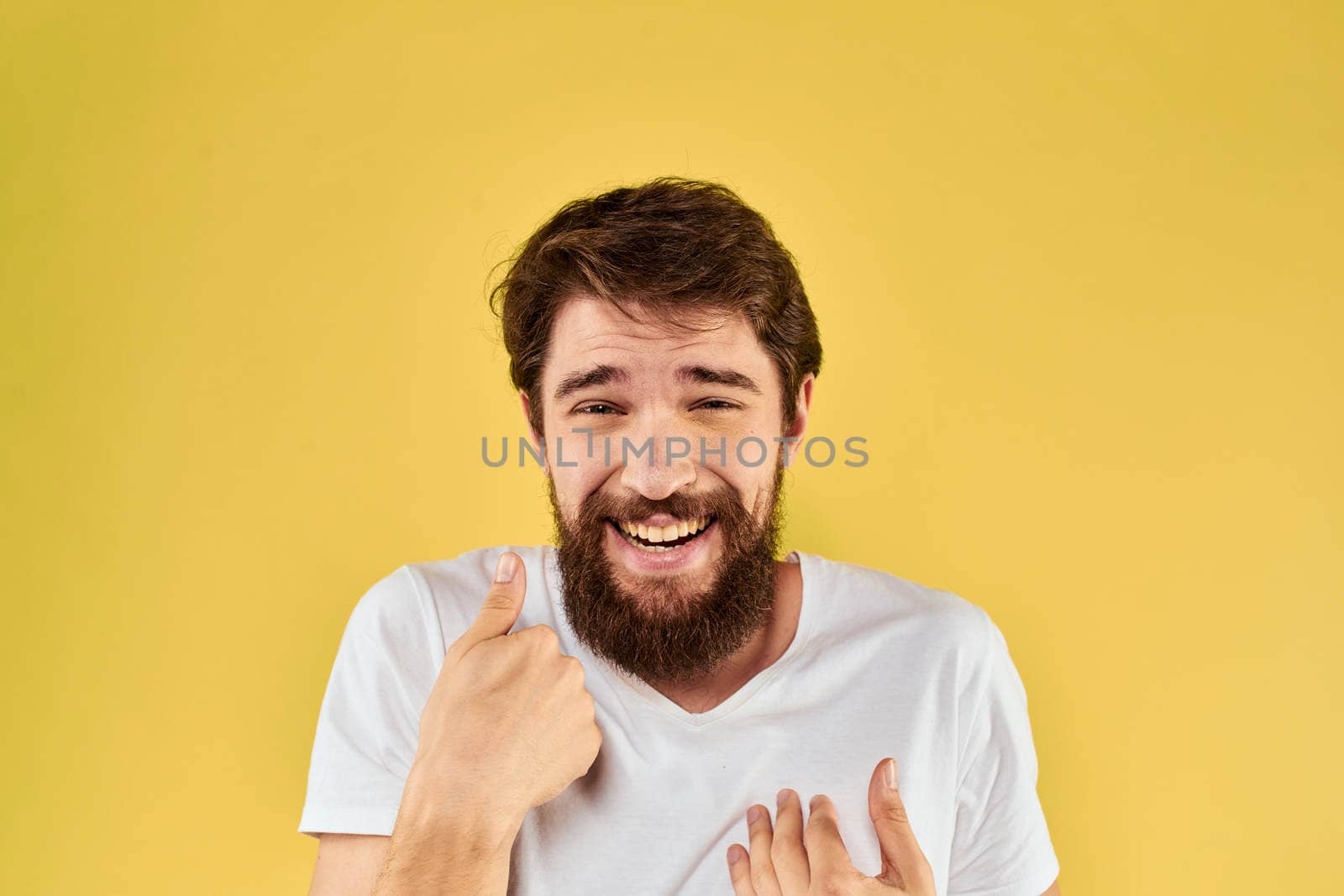 Bearded man emotions fun gesture with hands white t-shirt close-up yellow background. High quality photo