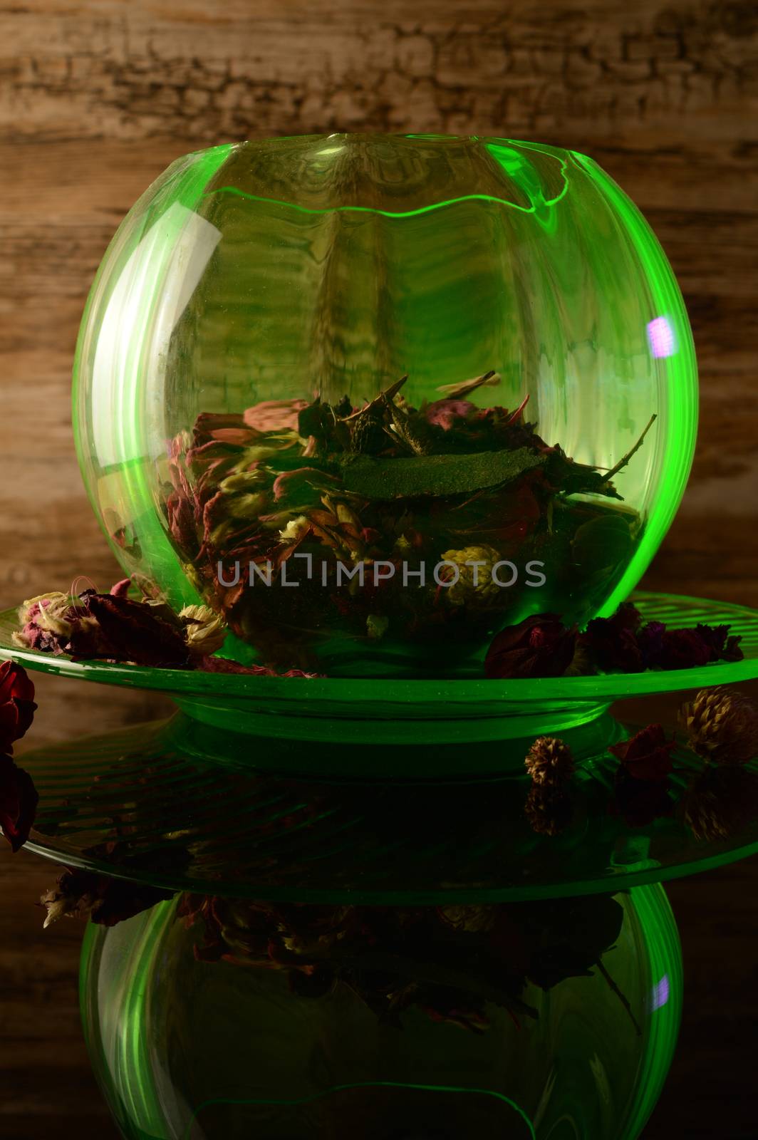 A uranium depression glass rose bowl under an ultraviolet light to reflect its bright green glow that is filled with aromatic potpourri flower mixture.