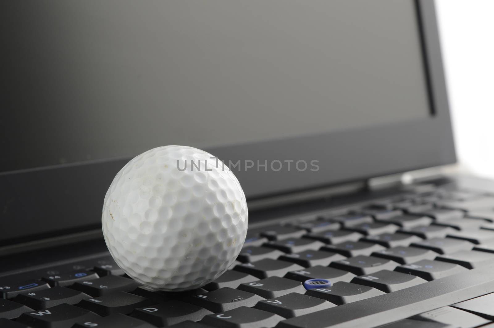 A golf ball on top of a laptop to make a descision of work or play.