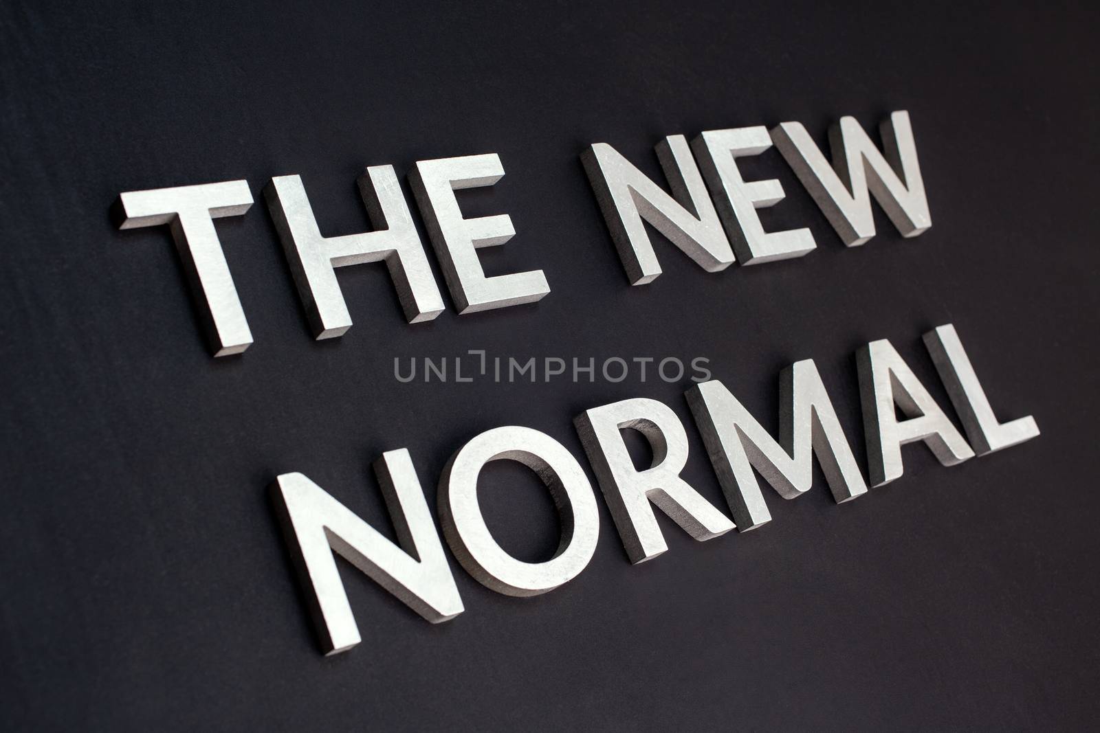 words the new normal laid with silver metal letters on flat black matte surface in tilted perspective with dark lightiing