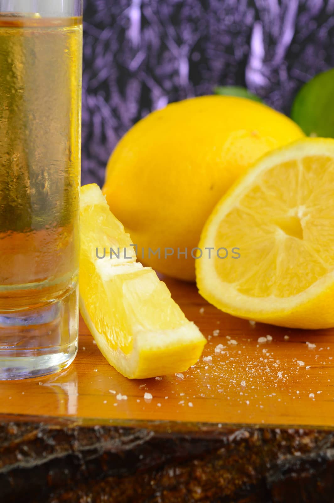 A vertical composition of a tequila shot ready with fresh cut lemon.