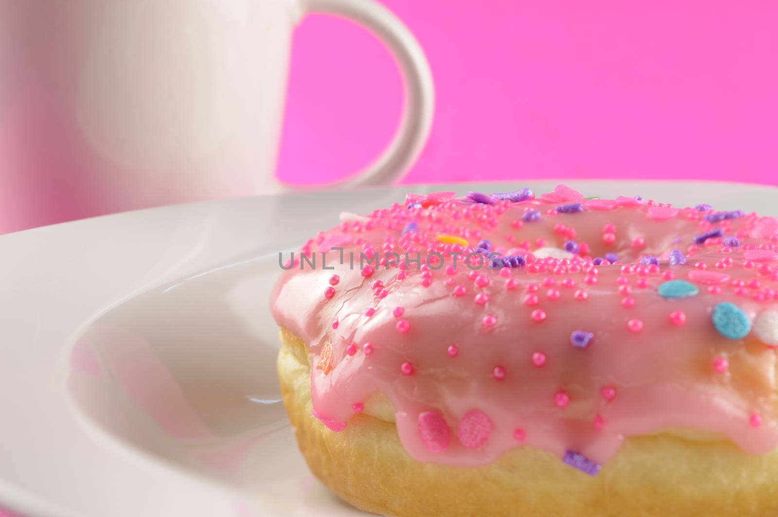 A low angle closeup of a freshly baked donut and coffee over a pink background.