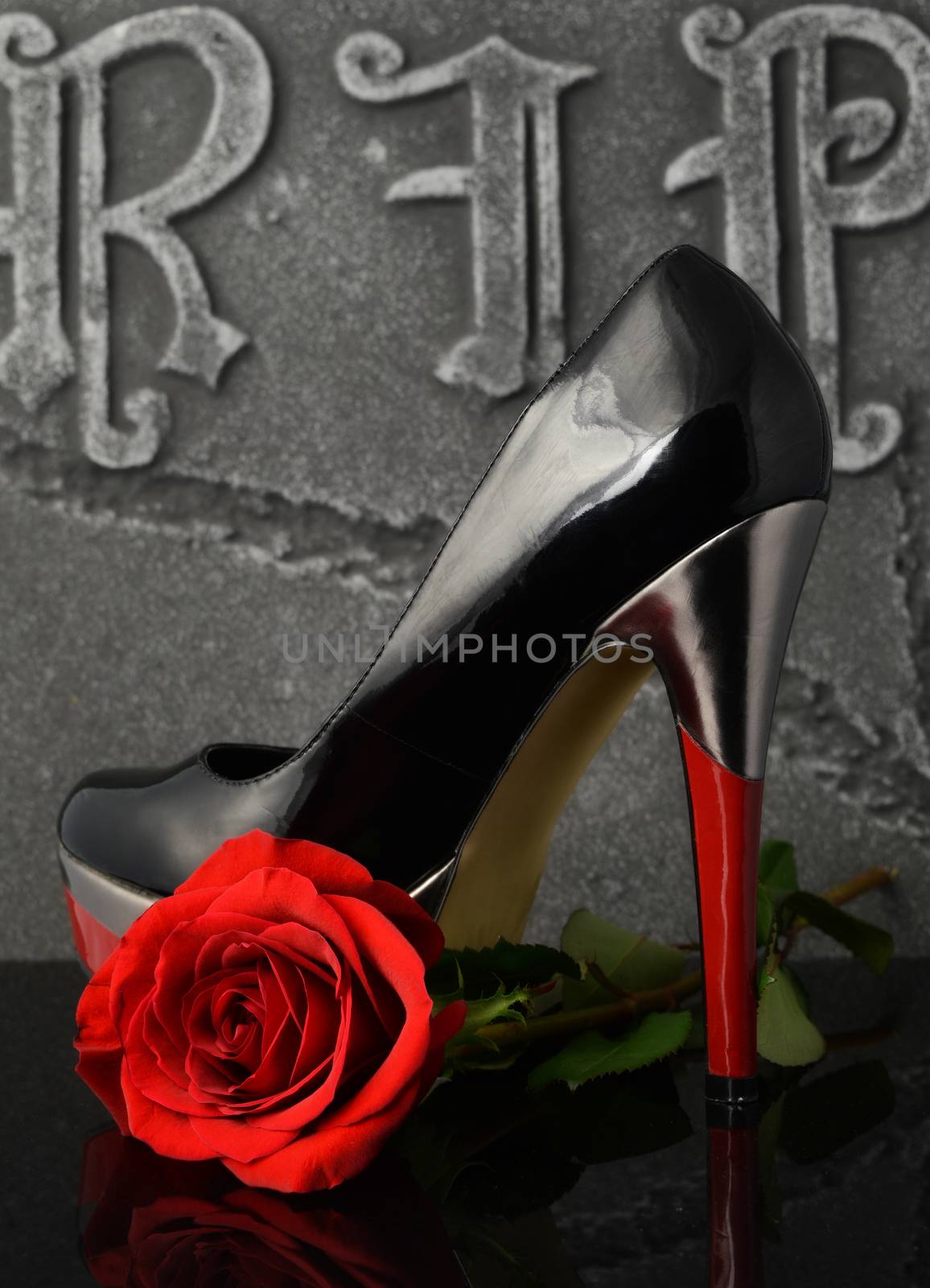 A womans shoe and red rose overtop of a gravestone to show respect for a lost loved one.