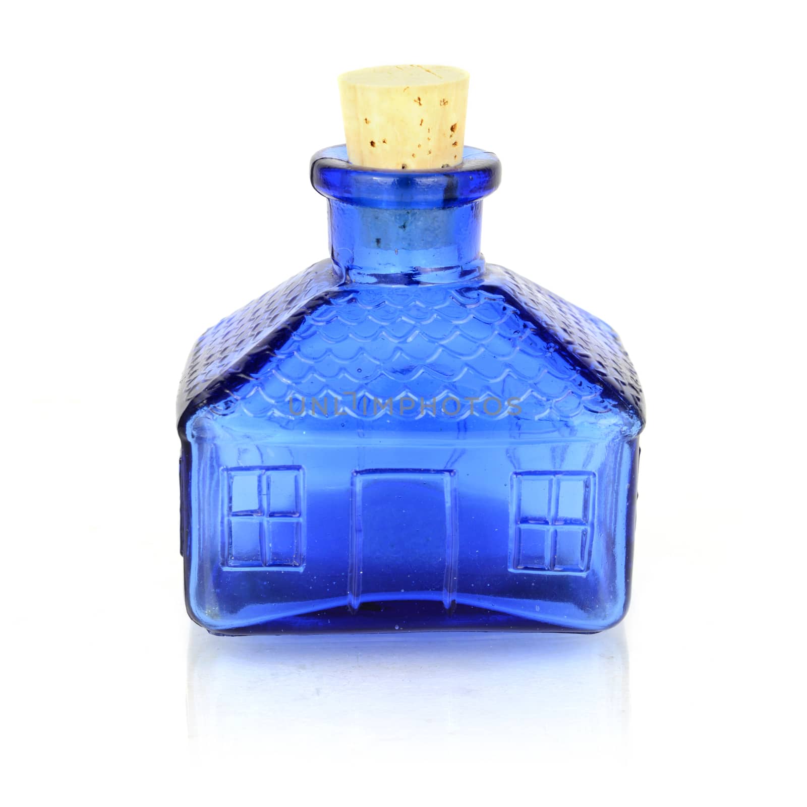 An isolated on a white reflective background image of an antique blue glass jar that is shaped like a house.