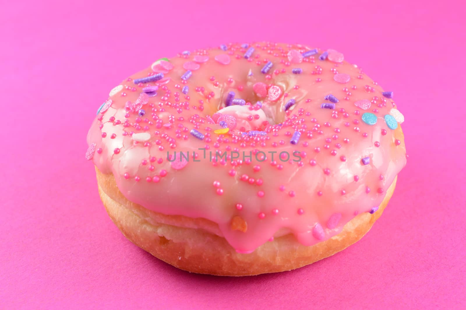 A freshly baked and frosted donut ov3er a pink background.