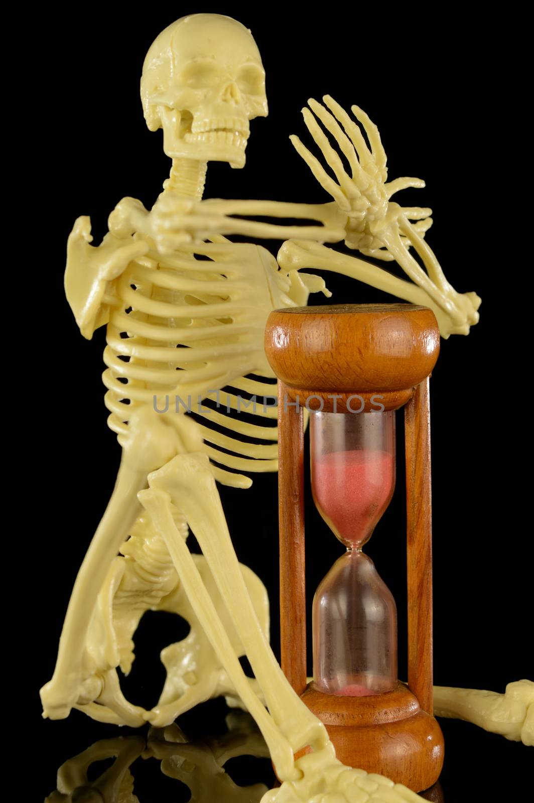 A human skeleton holds an hourglass with the sands falling closer to the end.