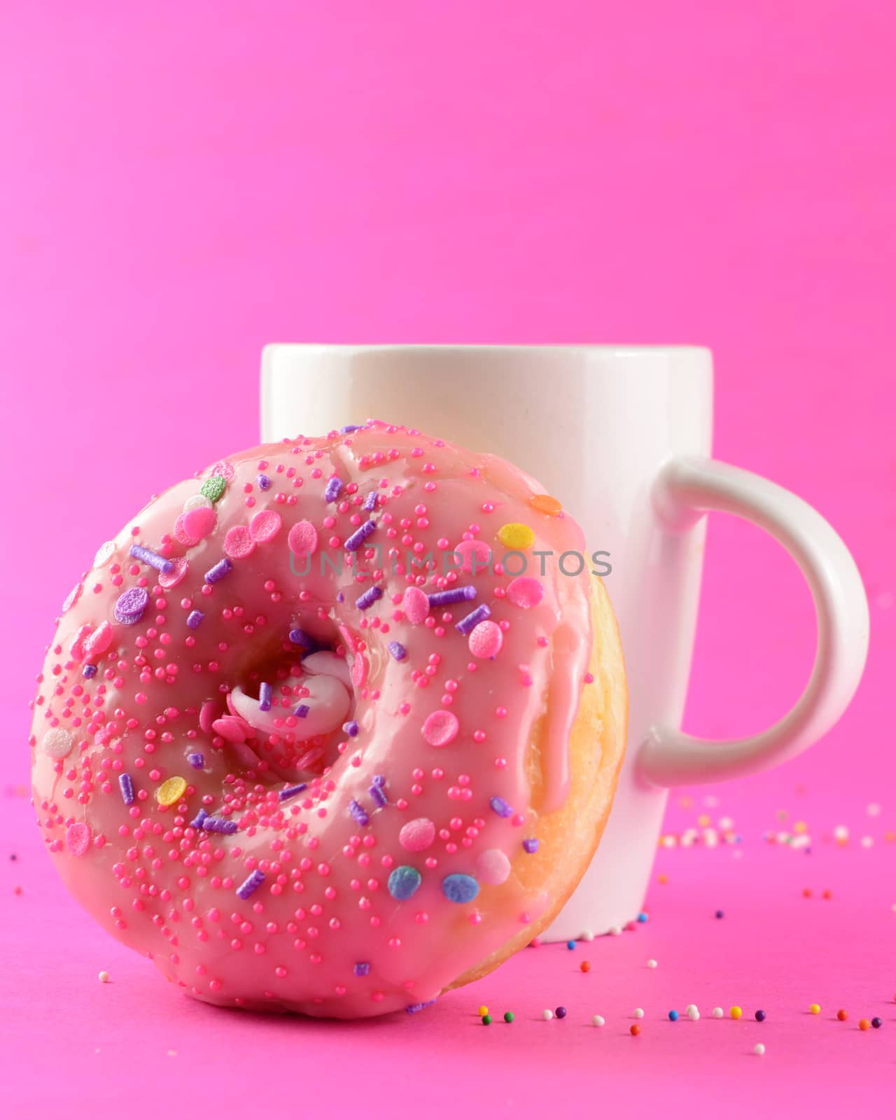 A coffee cup and donut over a pink background.