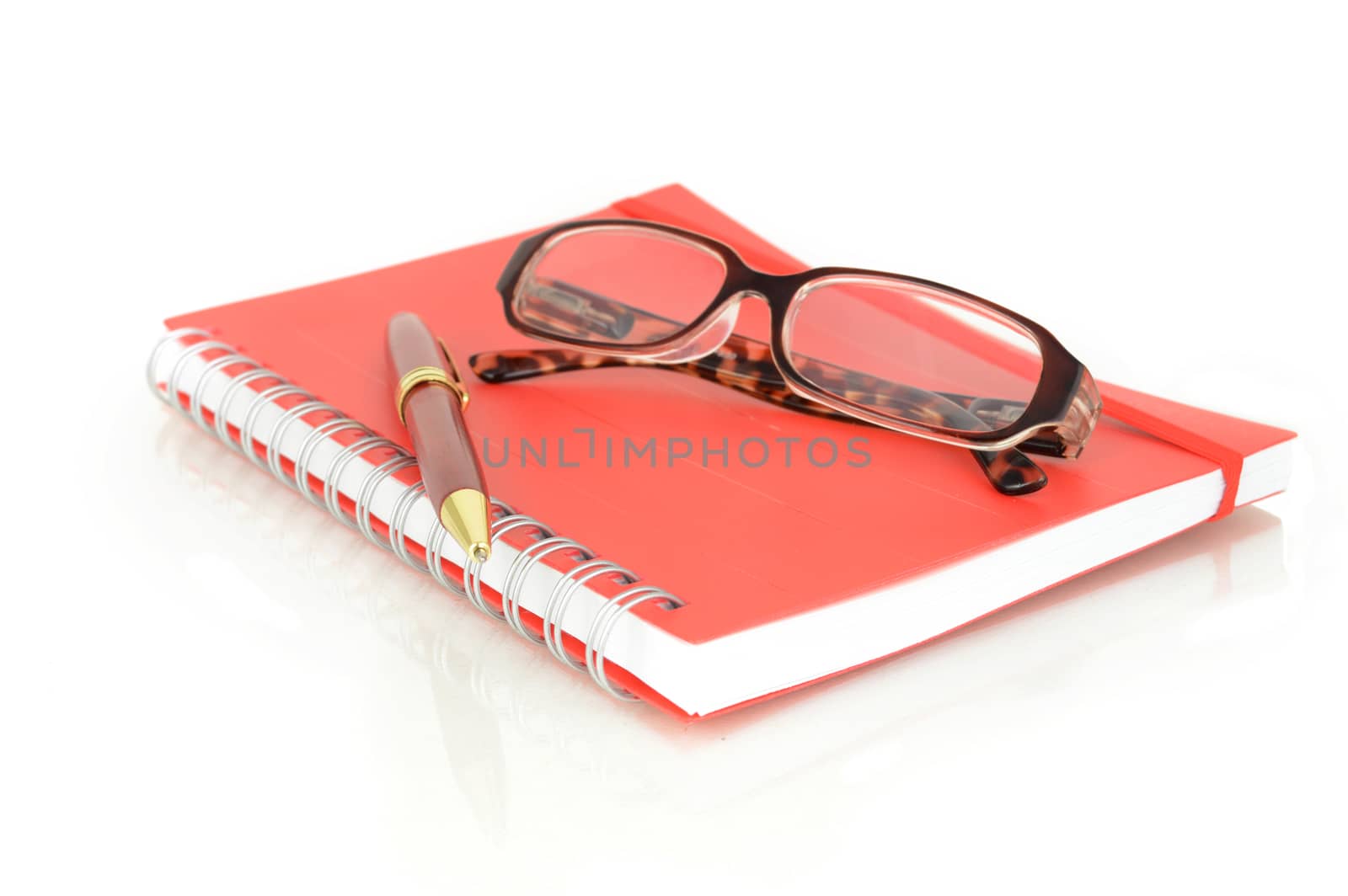 An isolated shot of a red notebook and pair of eye glasses over a white background.