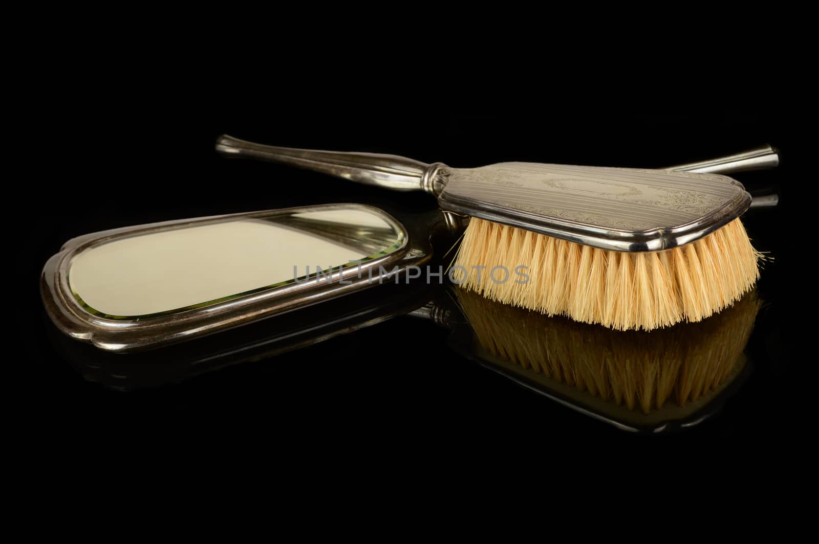 A vintage set of a handheld sterling silver mirror and hair brush isolated over a black reflective surface.