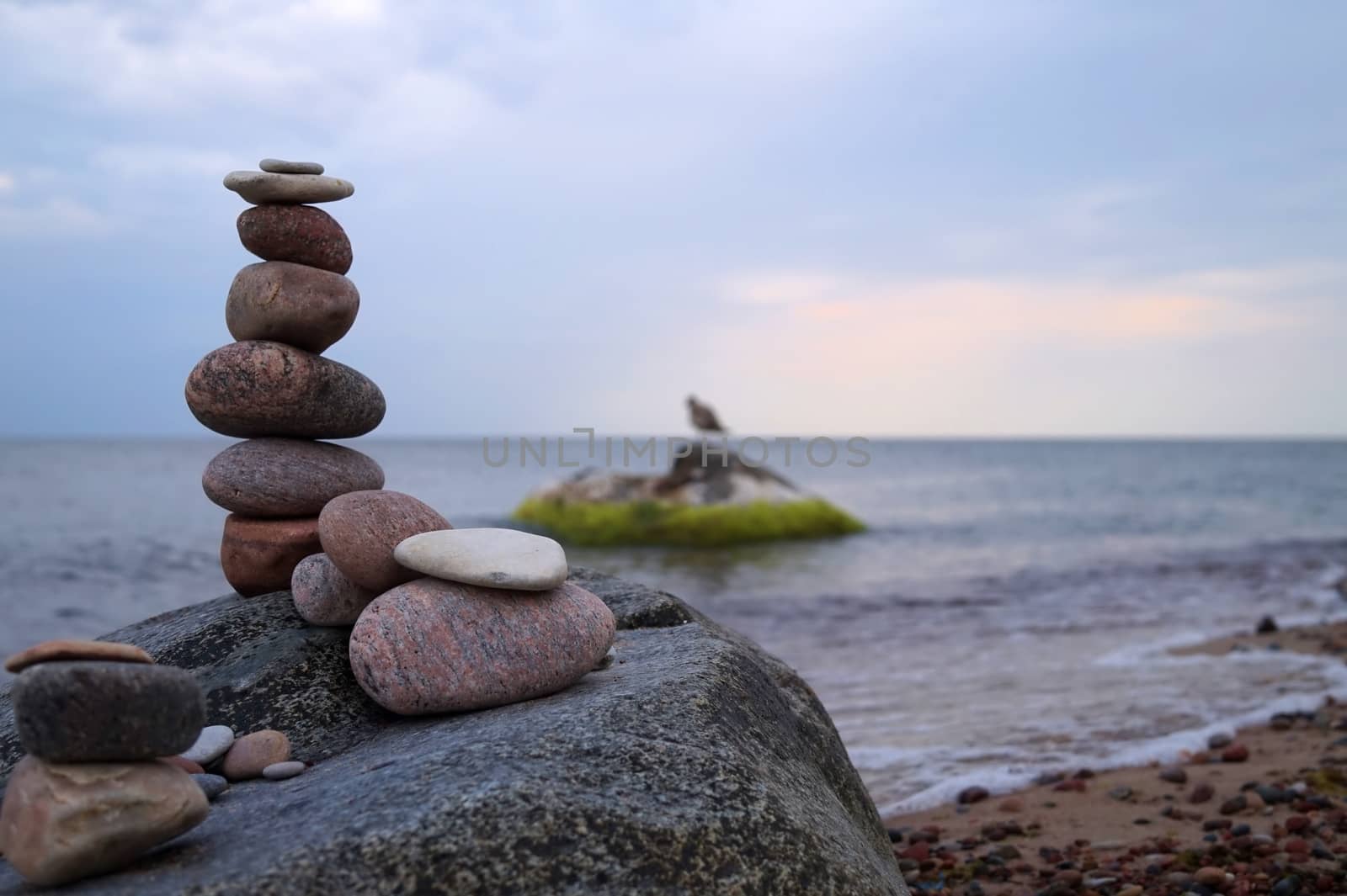 Tall balanced cairn of stacked of stones or rocks on a beach placed on top of a boulder overlooking the ocean and gentle waves at sunset