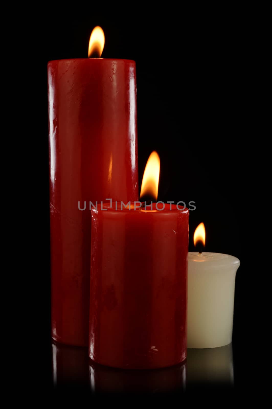 An isolated set of three candles lit over a black background.