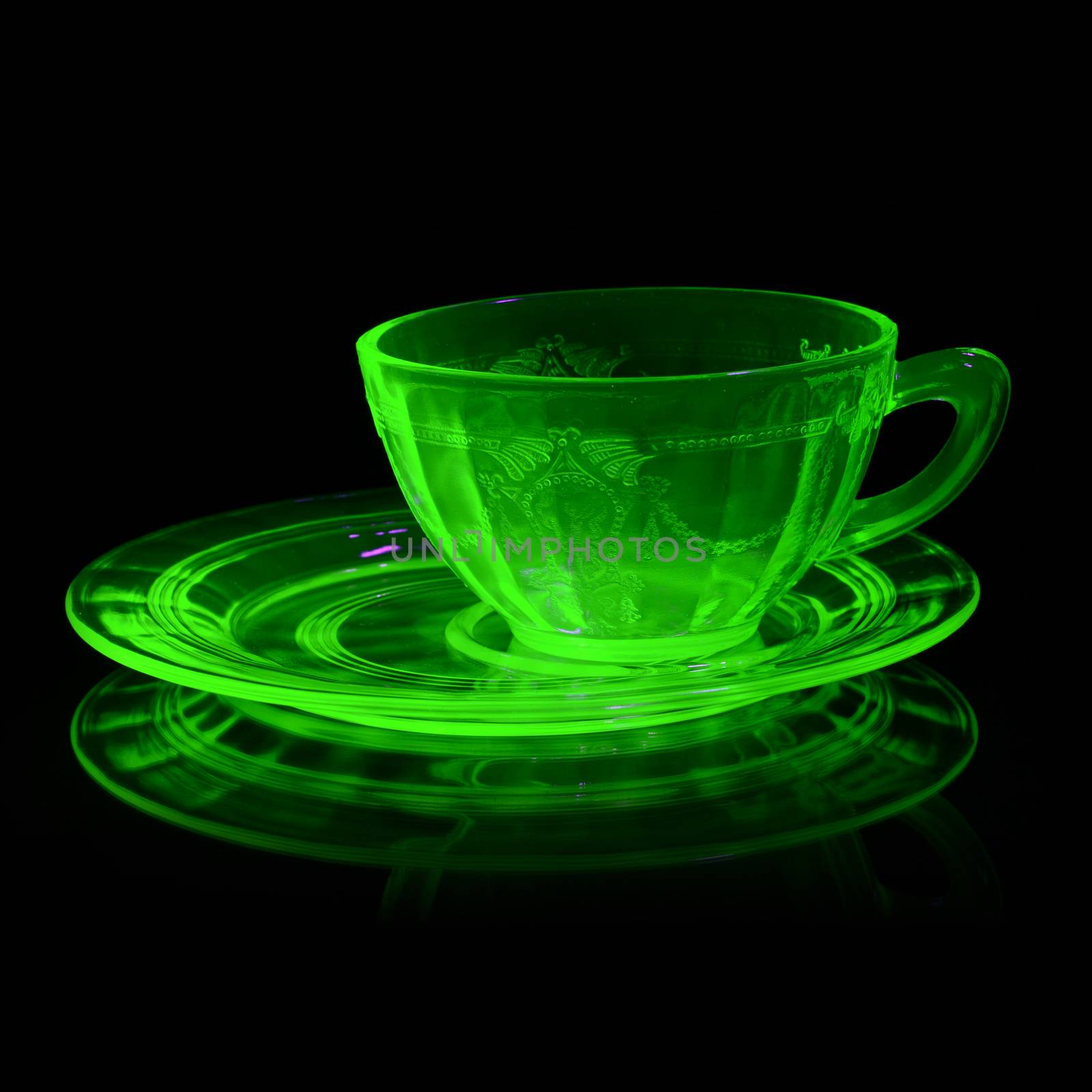 A glowing Uranium Glass Teacup and Saucer under Ultraviolet light to reveal its unique properties.