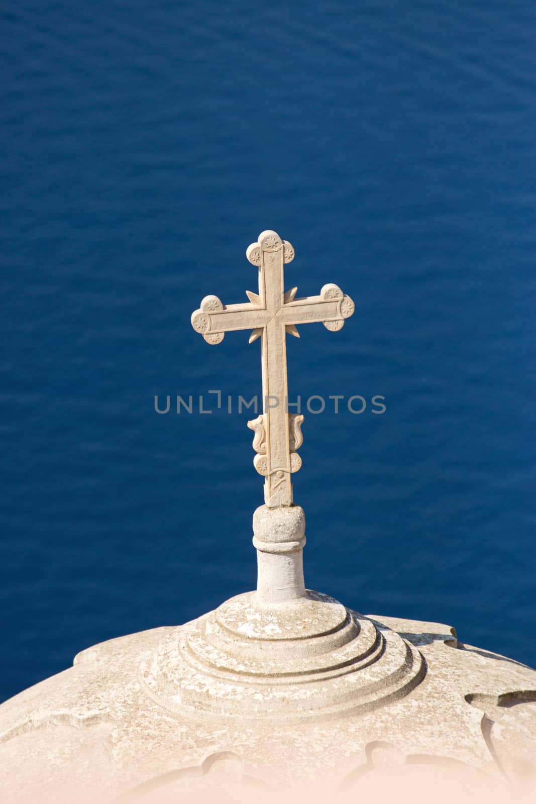 A roof of a church with a cross high up over the mediterranean sea, seen on Santorini island