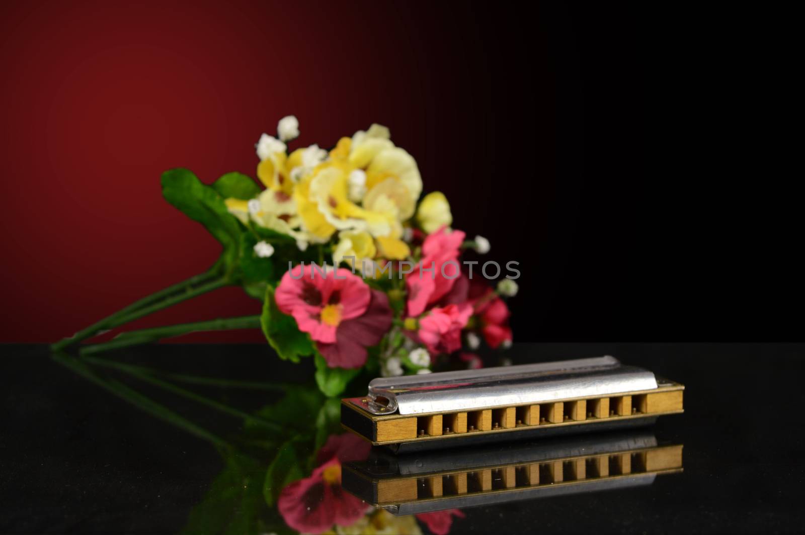 A closeup of a harmonica with a bouqet of flowers over a gradient background.