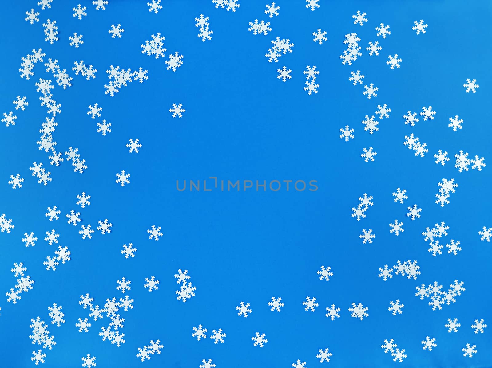 Scattered white snowflakes on blue background. Simple flat lay with copy space. Stock photo.