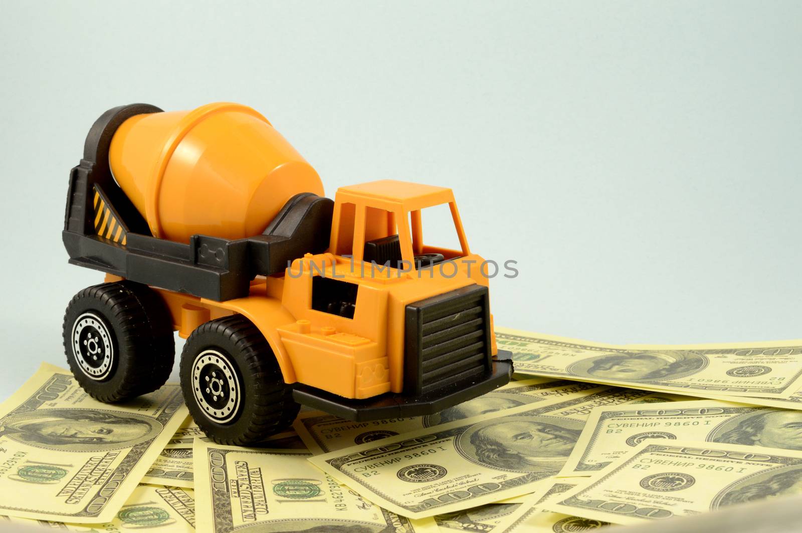 A scale model cement mixer truck over some banknotes for construction concepts.
