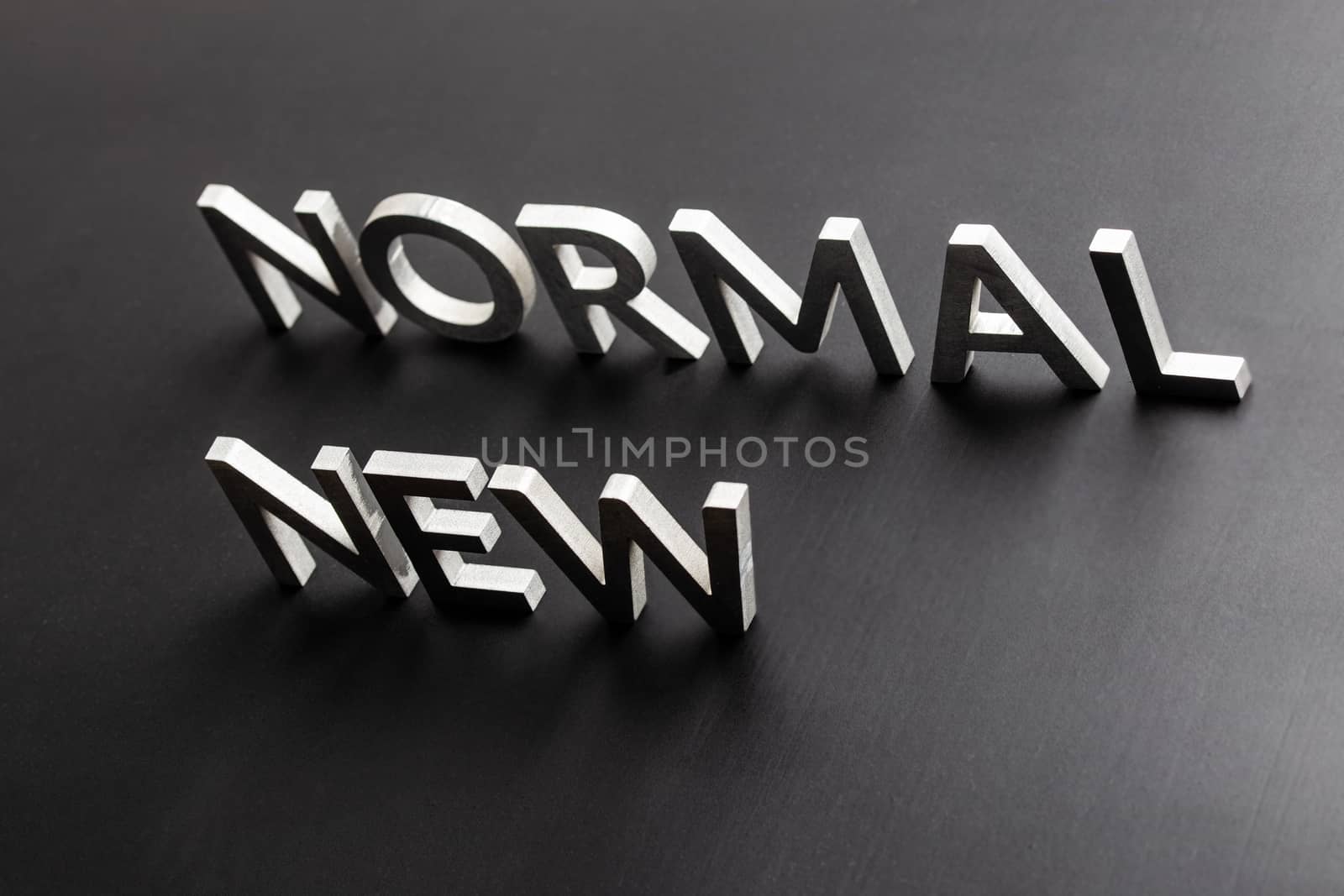 words new normal standing up with silver metal letters on flat black matte surface in tilted perspective with dark lightiing