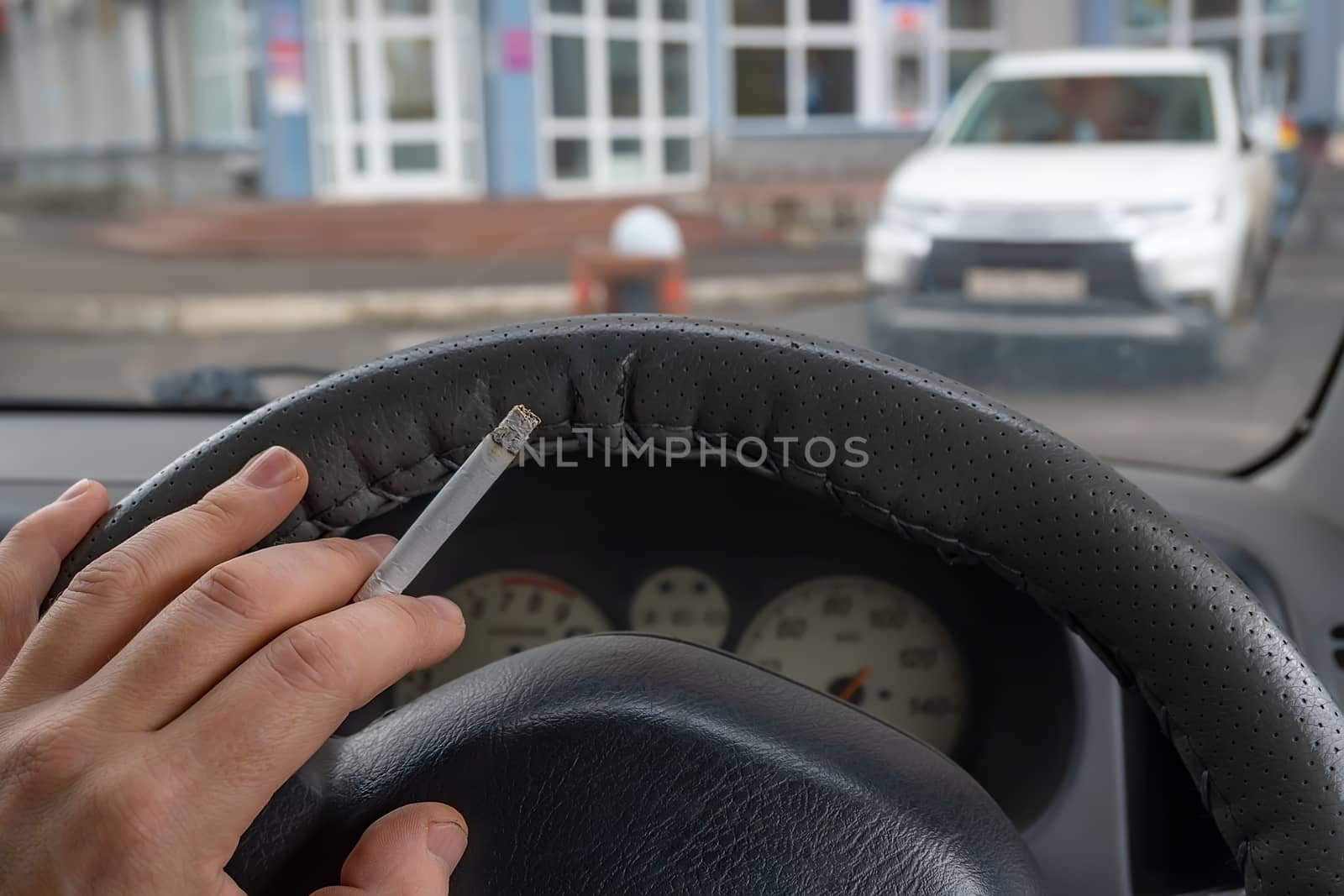 driver's hand with a cigarette on the steering wheel of the car by jk3030