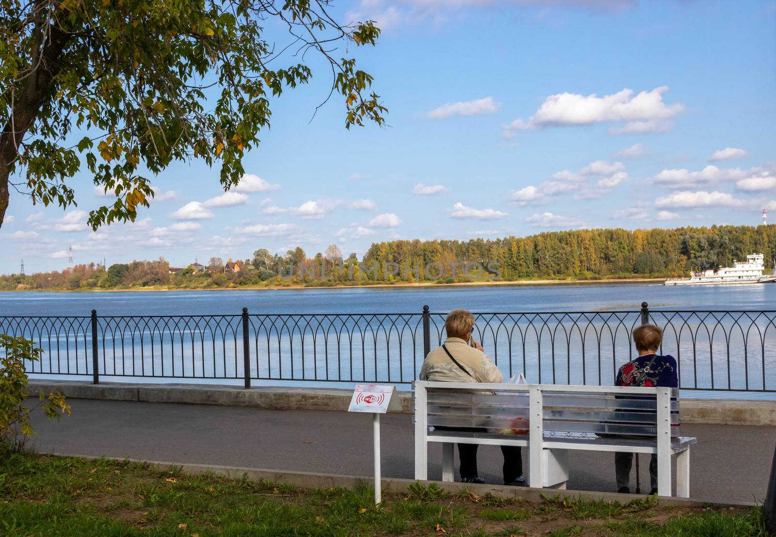 Two elderly women sit on a bench by the river in a city Park. Relaxation. The concept of loneliness by lapushka62