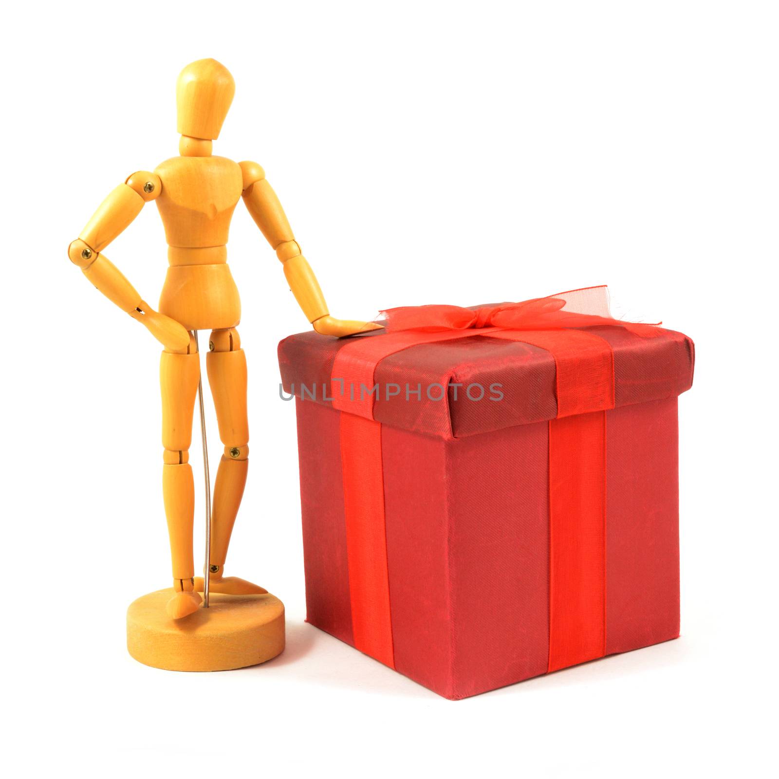 An isolated over a white background image of a wood artists figurine and a red gift box wrapped in ribbon.