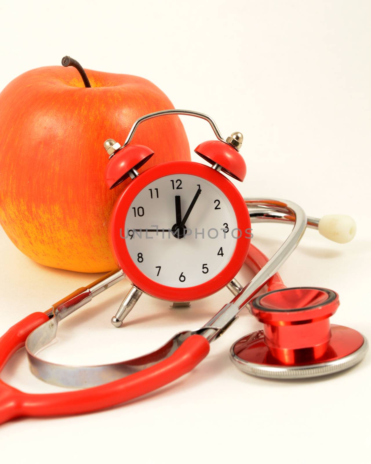 An apple and alarm clock and stethoscope come together for representing a clinical checkup time.