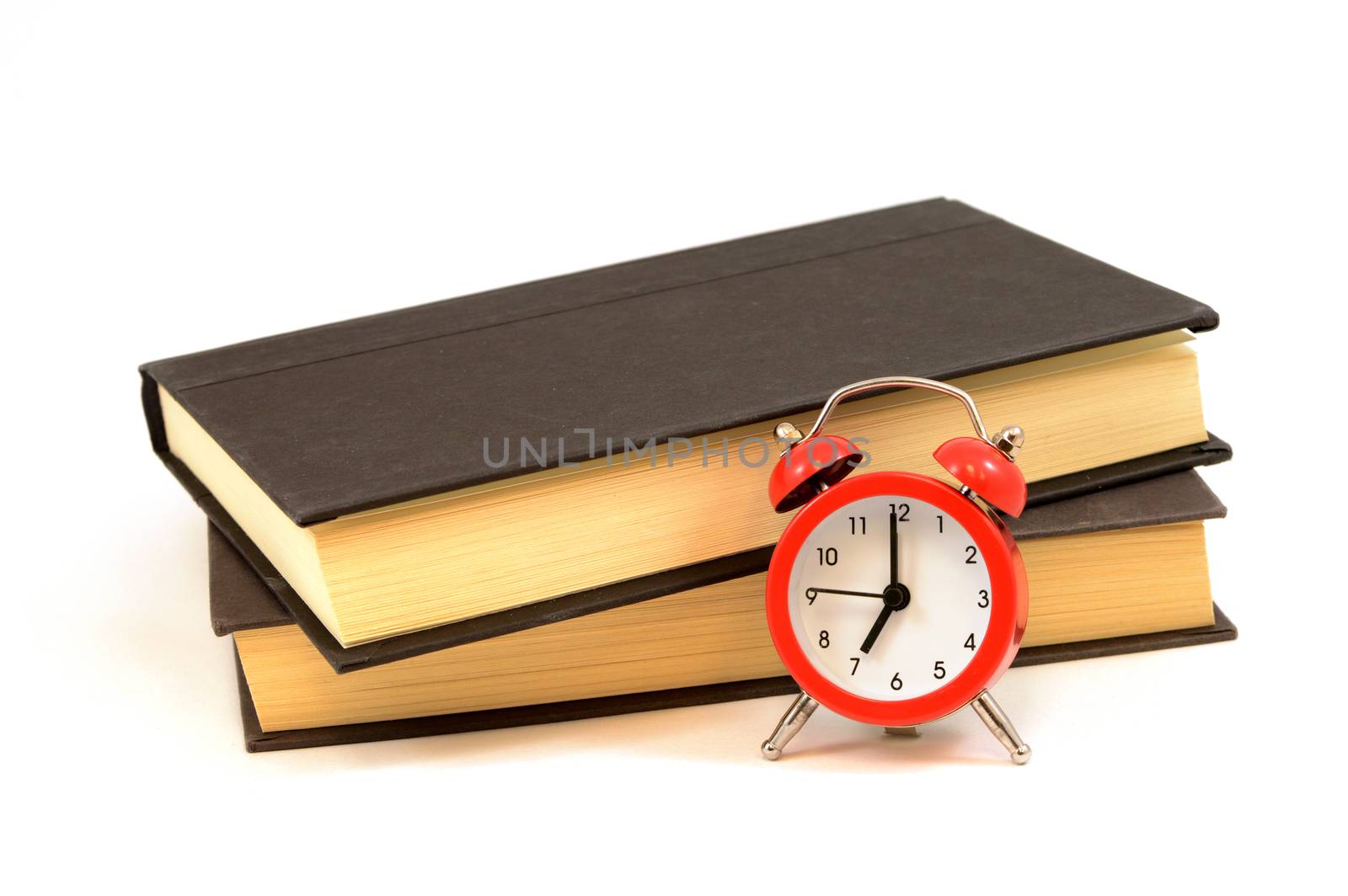 An isolated set of books with a red alarm clock.
