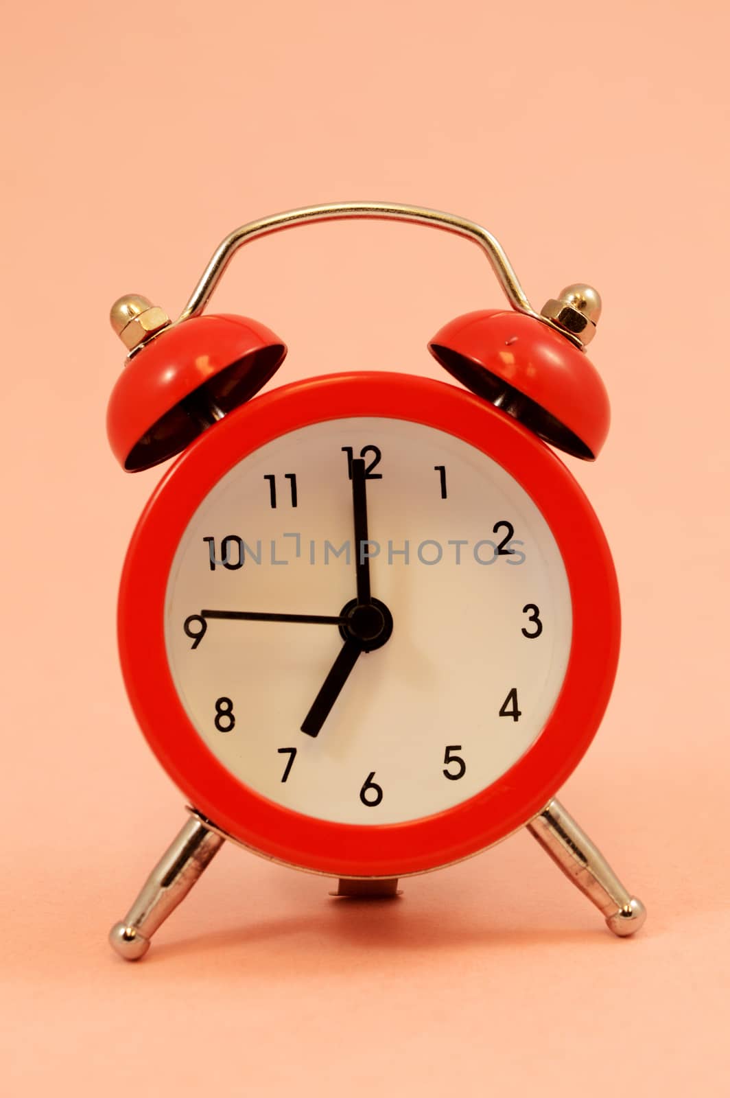 An isolated over pink background image of a red alarm clock set to seven oclock.