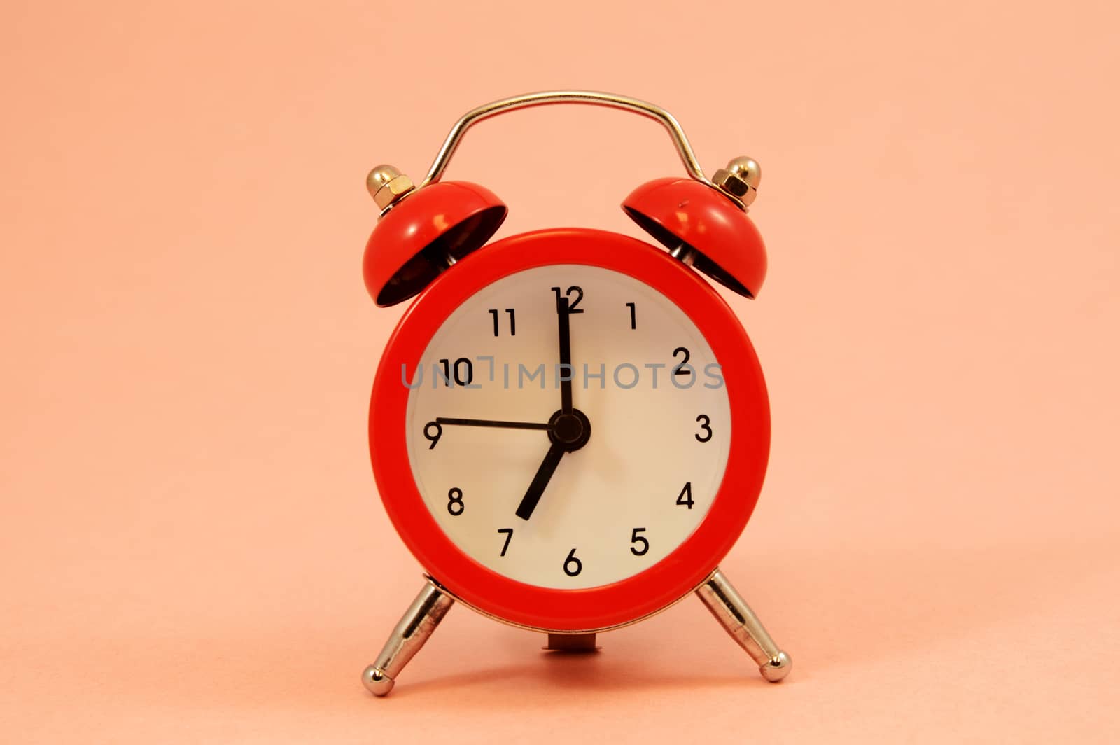 An isolated over pink background image of a red alarm clock set to seven oclock.