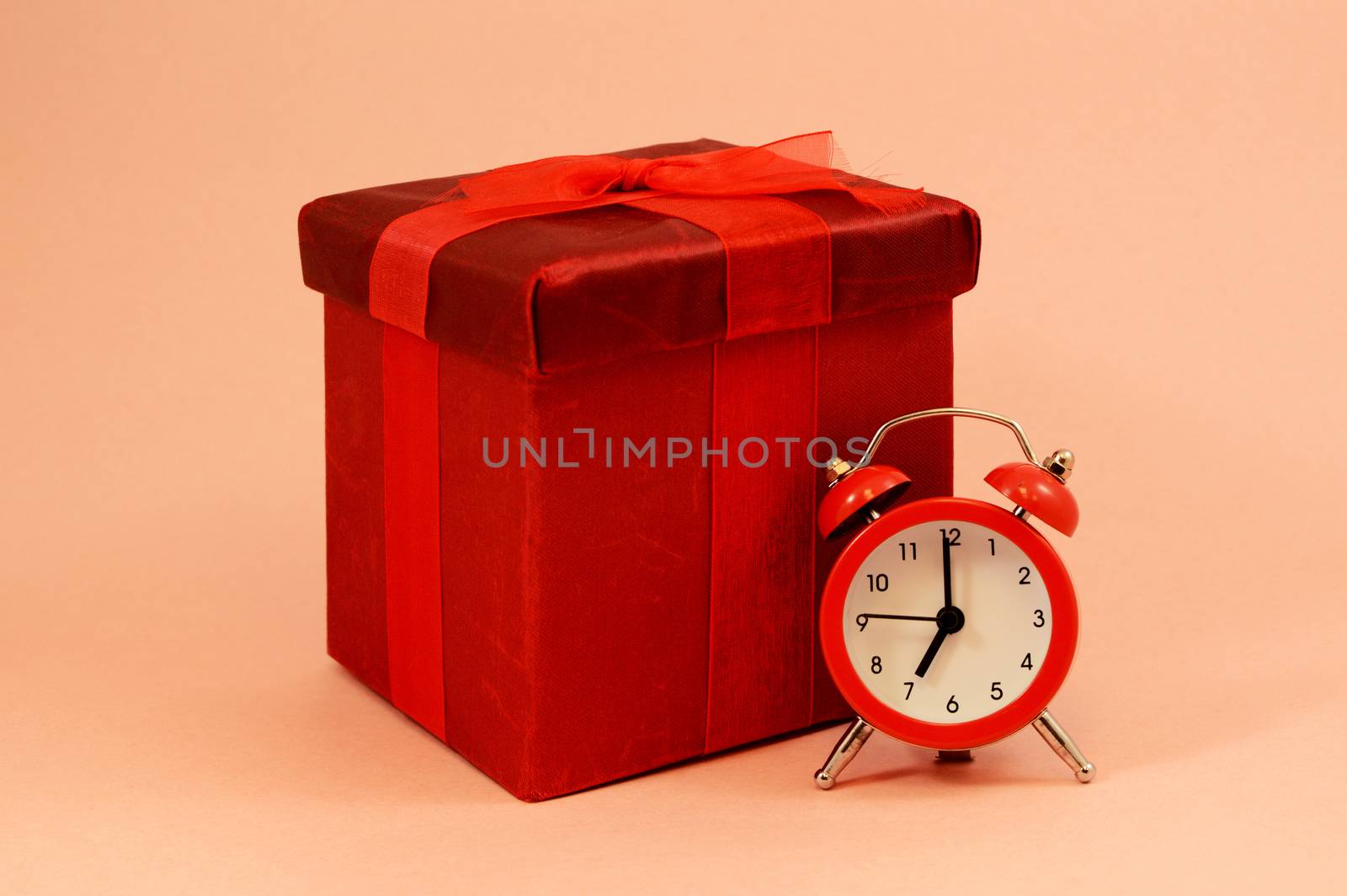 An isolated red gift box and alarm clock to represent that theres no time like the present.