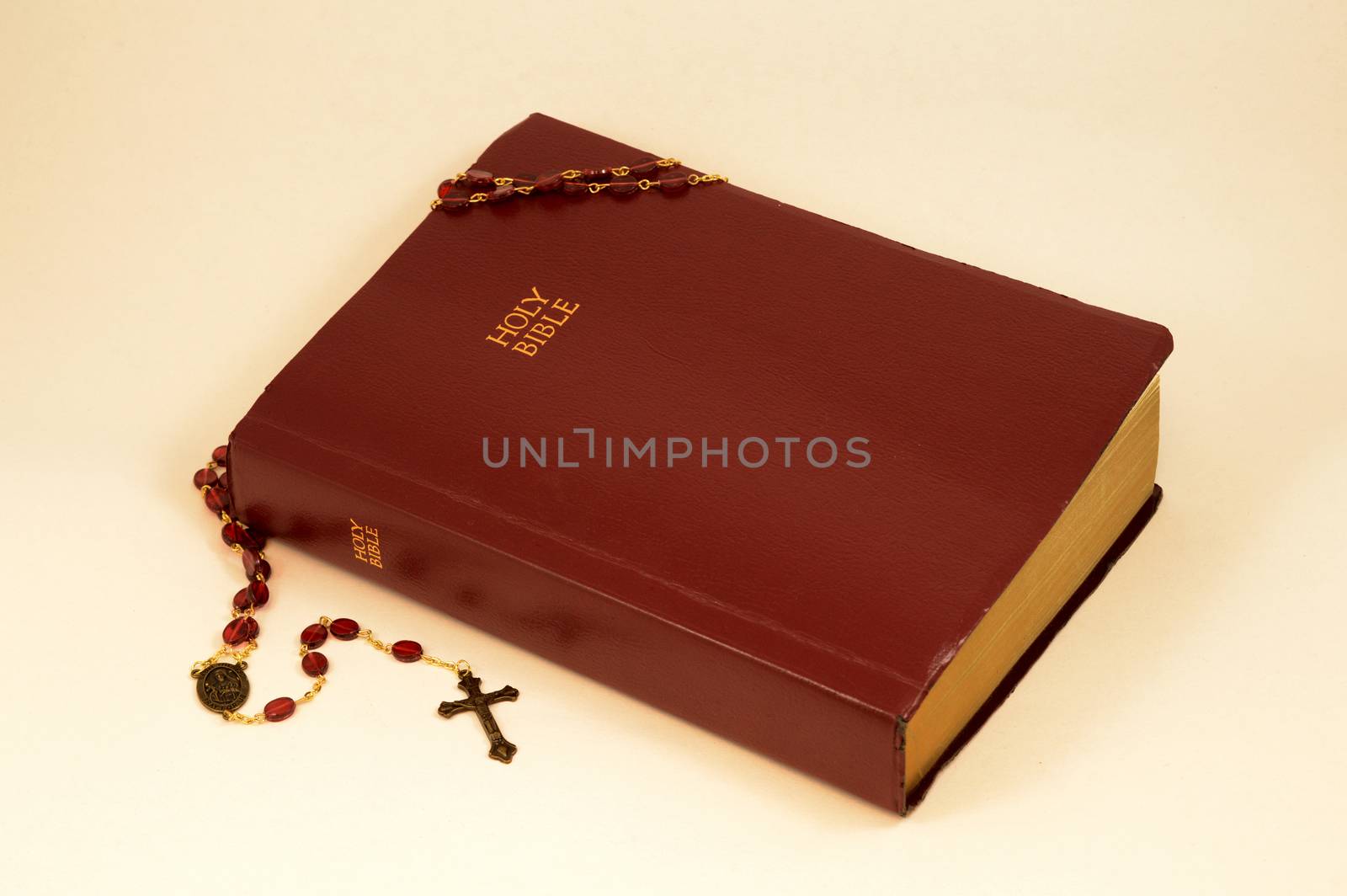 A closeup of the holy bible and rosary over a light pink background.