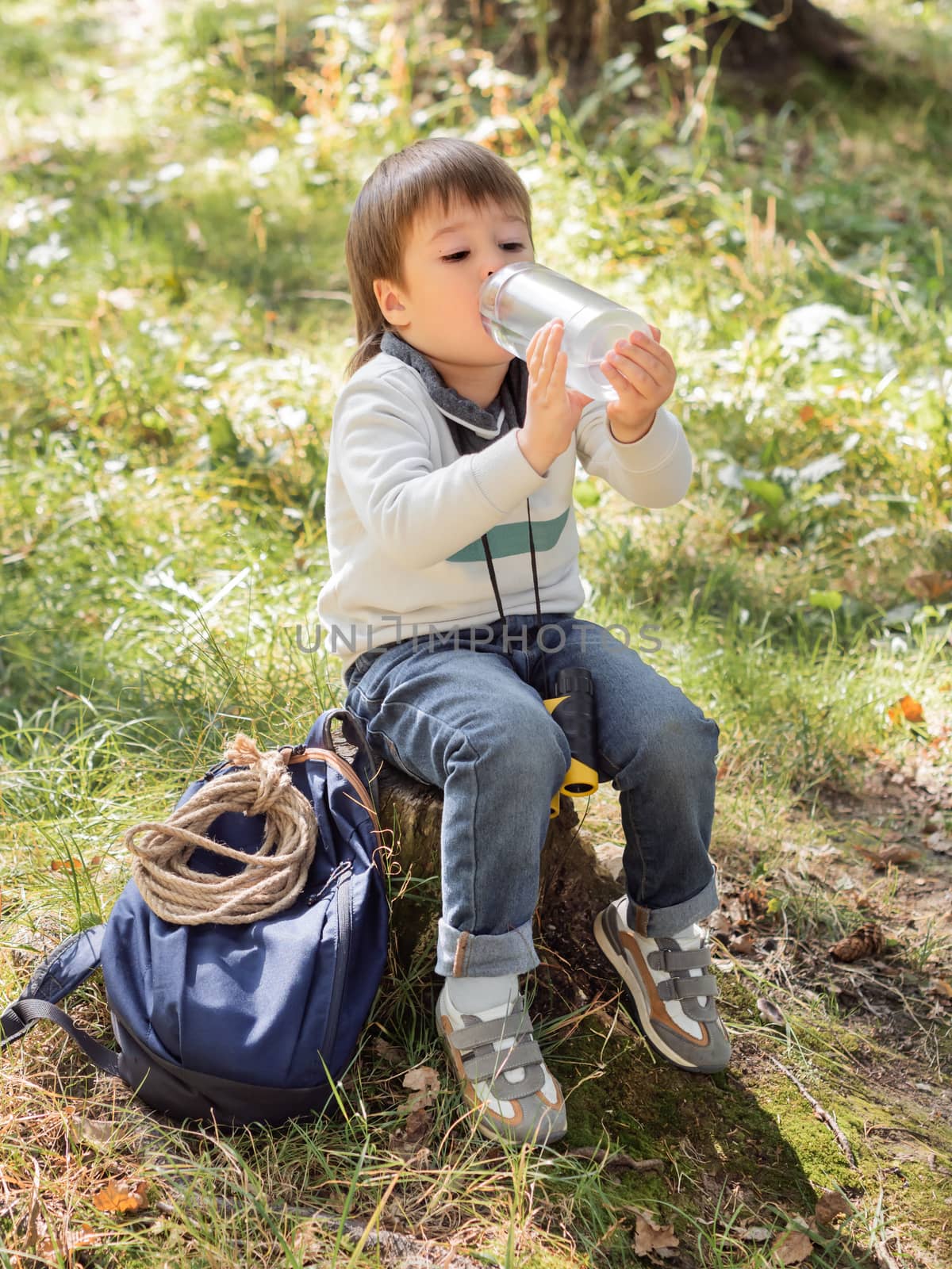 Little explorer on hike in forest. Boy with binoculars sits on s by aksenovko