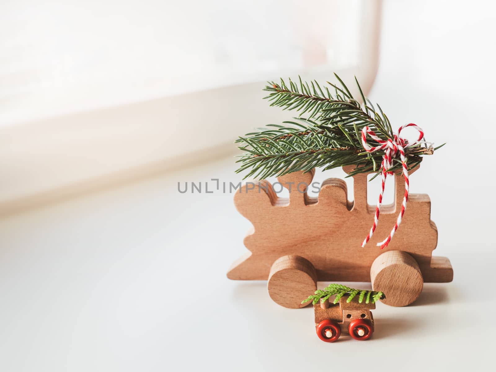 Two wooden trains with tied fir tree coniferous twigs. Dad and baby. Cute symbol of Christmas tree brought home for New Year celebration. Winter holiday spirit. Copy space.