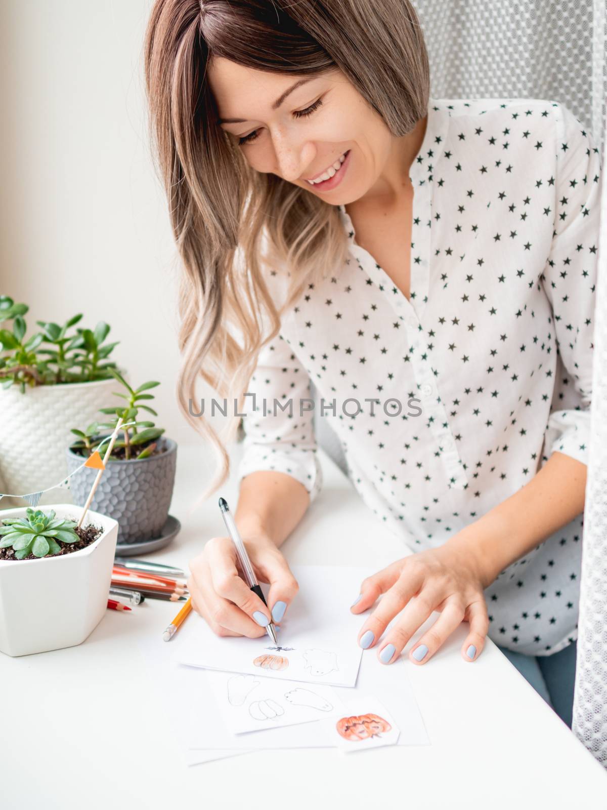 Woman decorates flower pots with handmade Halloween stickers. Hand drawn ghosts, flags and pumpkins in flower pot with succulent plant.