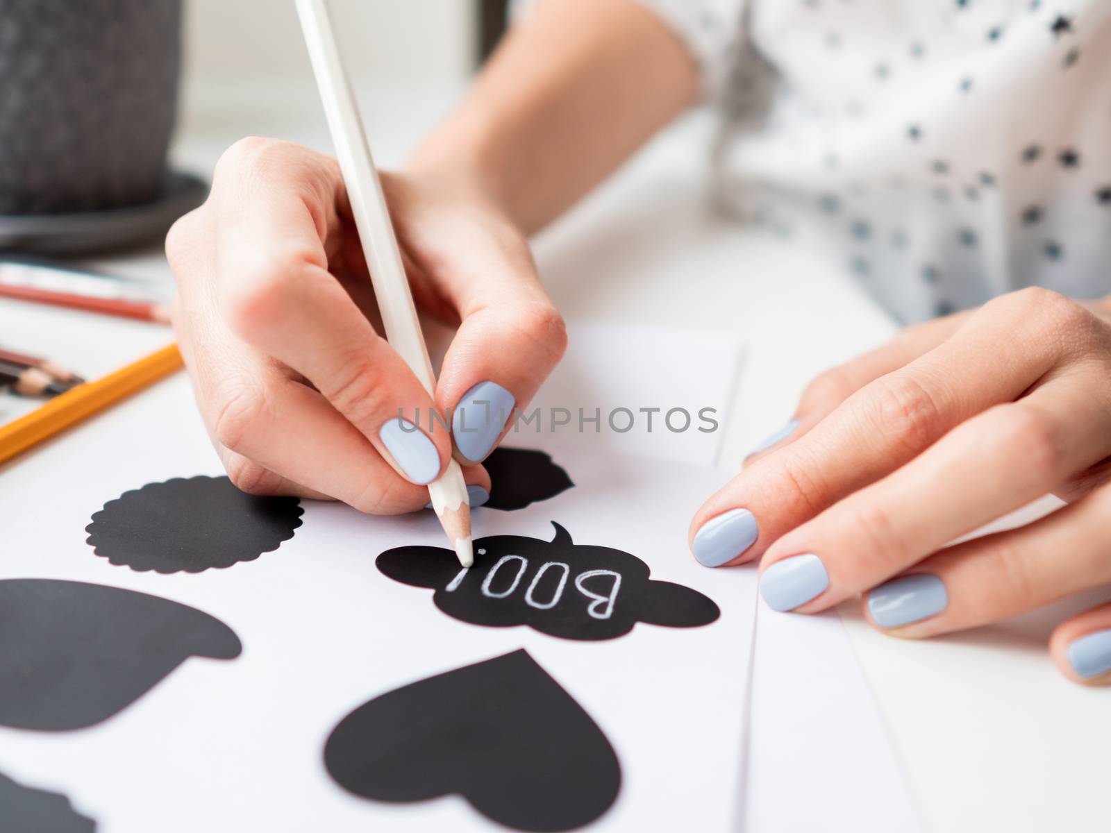 Woman writes Boo! on decorative black stickers for flower pots. Handmade decorations for Halloween.