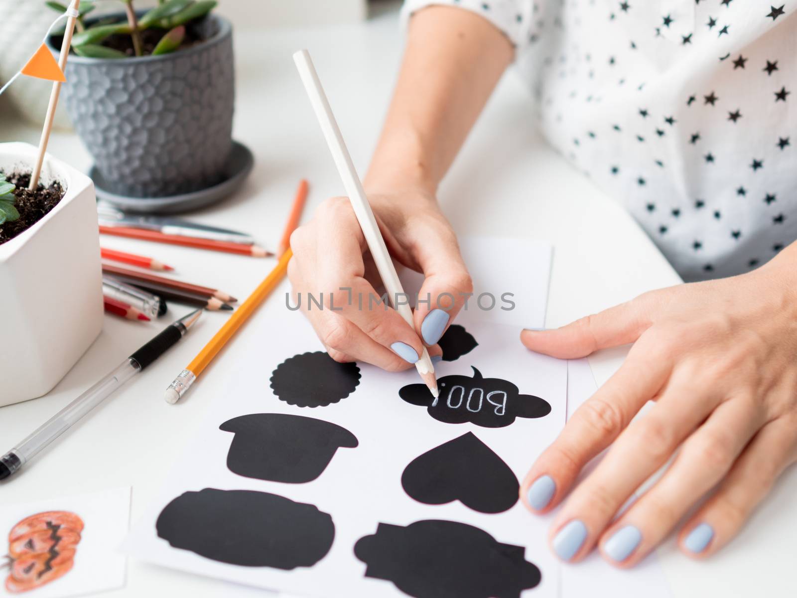 Woman writes Boo! on decorative black stickers for flower pots. by aksenovko